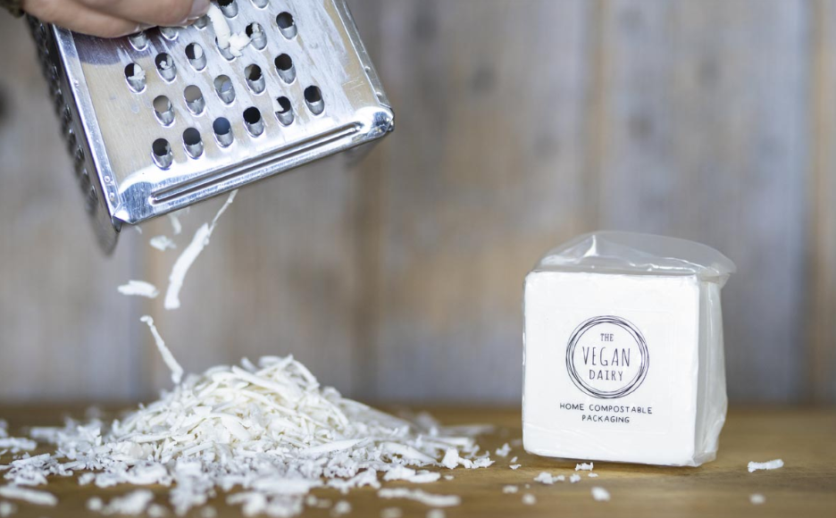 person grating cheese with block of Vegan Dairy cheese on the side